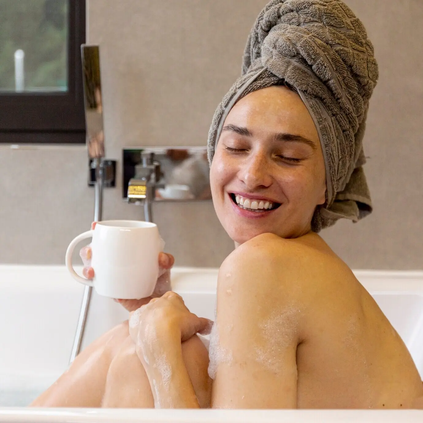 Seitenansicht einer glücklichen Frau mit einer Tasse in der Badewanne.