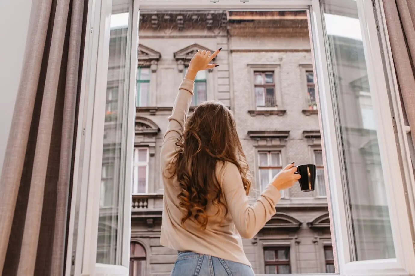 Innenraum-Porträt in Rückenansicht eines schlanken Mädchens mit langen lockigen Haaren, das Jeans trägt.